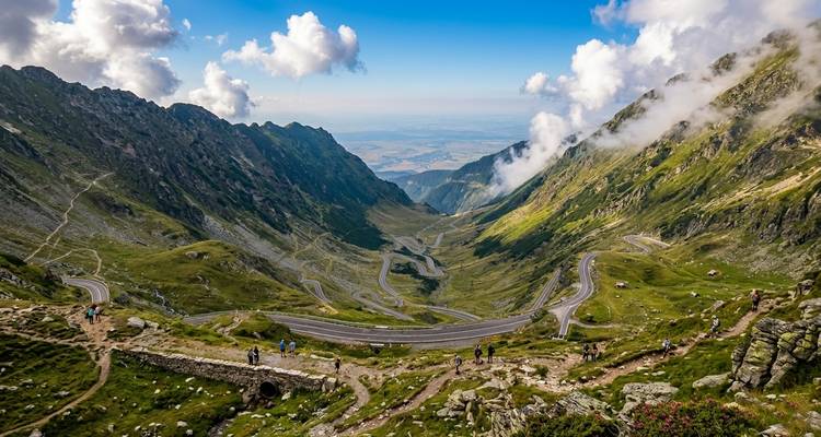 Weids luchtbeeld van de slingerende Transfăgărășan Highway die door groene Karpaten snijdt onder voorbijdrijvende wolken