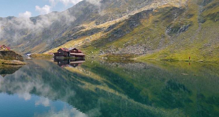 Spiegelachtig alpenmeer dat mistige bergen en verspreide chalets weerkaatst op een bewolkte ochtend