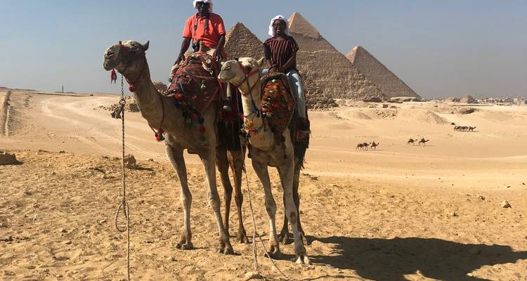 People riding camels in front of pyramids