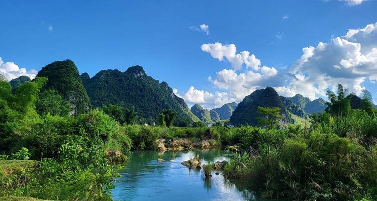 Río azul cristalino serpenteando entre picos afilados de piedra caliza kárstica bajo un cielo luminoso con nubes dispersas.