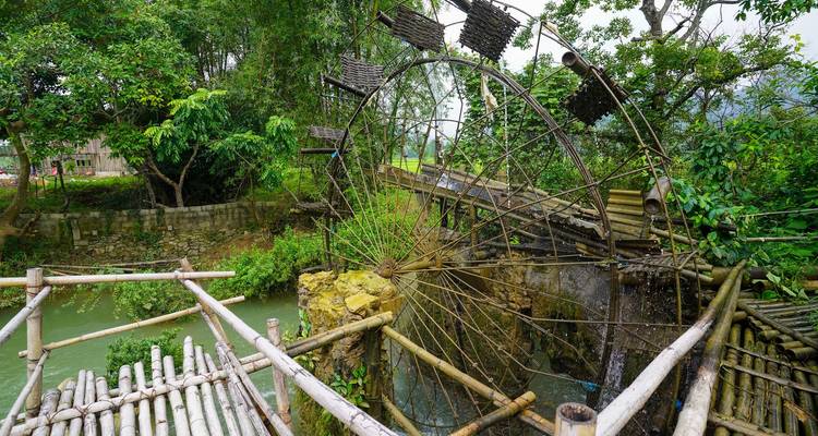 Rueda de agua tradicional de bambú y canales de madera junto a un arroyo verde en el Vietnam rural.