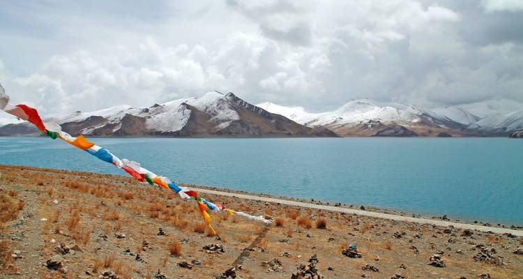 Une vue à couper le souffle d'un lac avec des drapeaux de prière colorés au premier plan et des montagnes enneigées en arrière-plan.