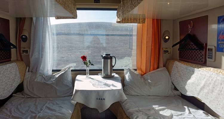 Intérieur d'une cabine de train avec une table dressée d'une théière et d'une tasse, sous la lumière du soleil filtrant par la fenêtre.
