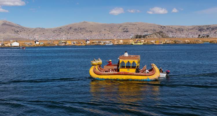 Una lancha de junco amarillo brillante con proa en forma de cabeza de dragón se desliza por las aguas azul profundo del Lago Titicaca.