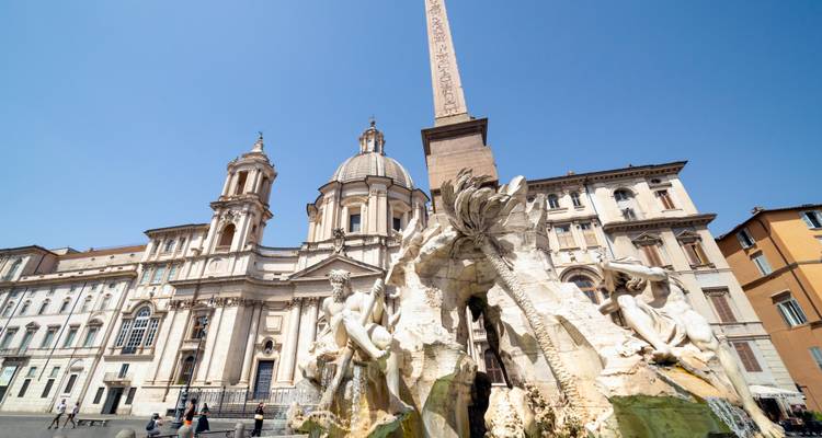 Fontana dei Quattro Fiumi en la Piazza Navona con la iglesia de Sant'Agnese in Agone bajo un cielo azul despejado en Roma.