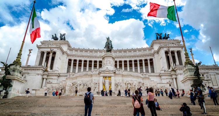 Monumento Gran Altare della Patria en Roma con banderas italianas ondeando y visitantes subiendo por la amplia escalinata.