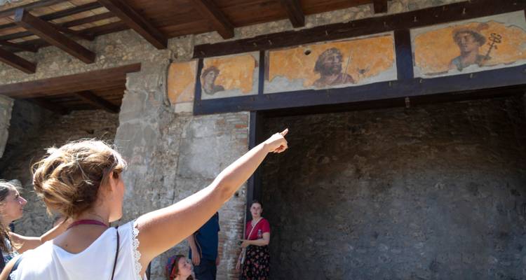 El guía señala hacia frescos antiguos dentro de una ruina de piedra mientras los visitantes escuchan.