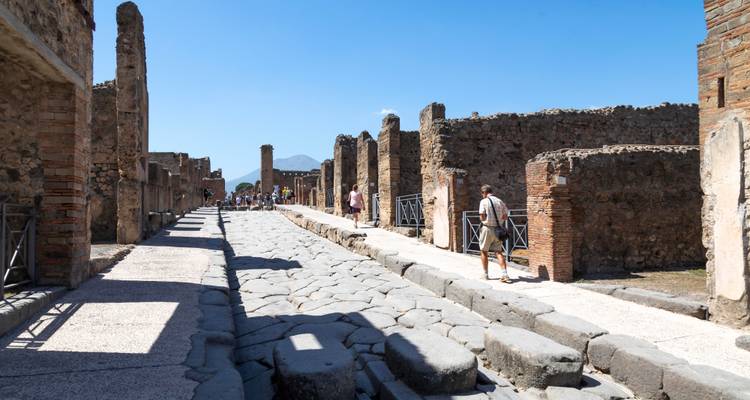 Calle romana pavimentada con piedra flanqueada por muros en ruinas en Pompeya bajo un cielo radiante.