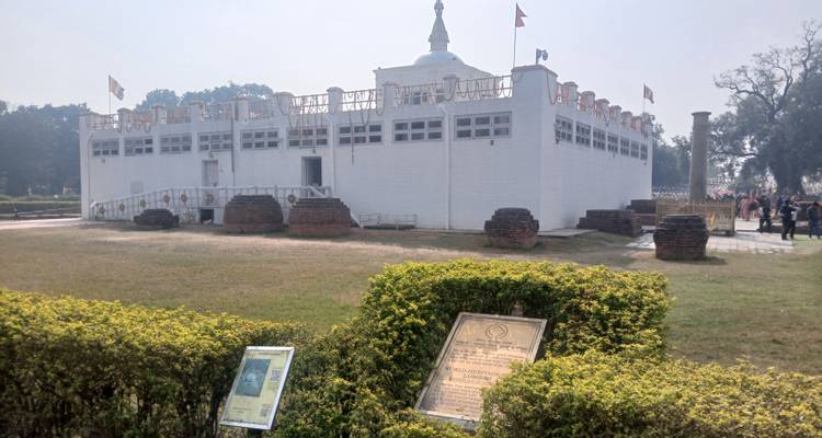 Pilger besuchen die Weiße Stupa mit Beschilderung im Vordergrund.