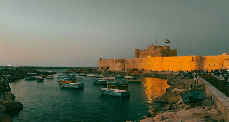 Boote schaukeln im Hafen neben den sonnendurchfluteten Mauern der Zitadelle von Qaitbay in Alexandria in der Dämmerung.