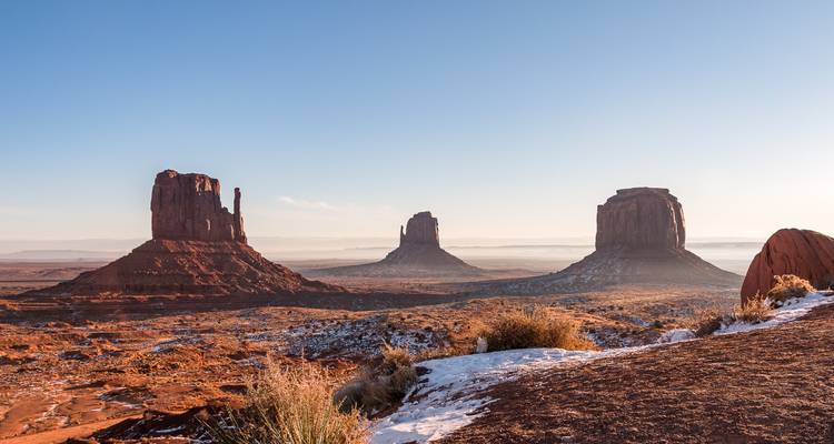 Los icónicos buttes se elevan desde el suelo del desierto de arena roja del Valle de los Monumentos bajo un cielo pálido de la mañana.