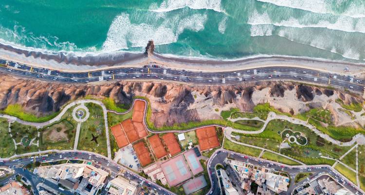 Aerial view of a coastal cityscape with roads and green parks.