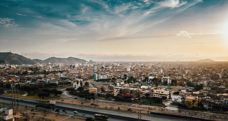 Cityscape at sunset with a sprawling urban area and hills.