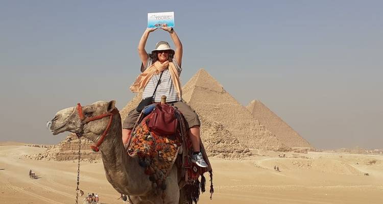 Toerist bovenop een kameel voor de piramides van Gizeh, met een bord in de hand.