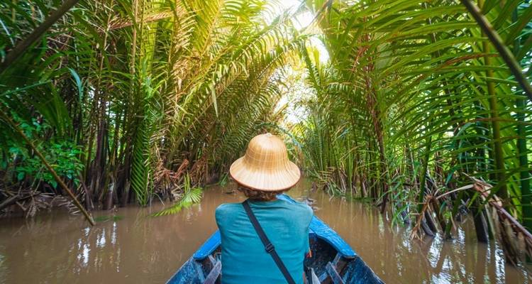Person rowing a boat through narrow water channels lined with trees