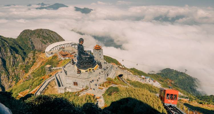 Massive statue de Bouddha en bronze sur la montagne Fansipan émergeant au-dessus d'une mer de nuages et d'une route de téléphérique.