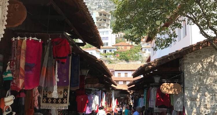 People walking between stalls in a lively outdoor market surrounded by textiles and crafts.