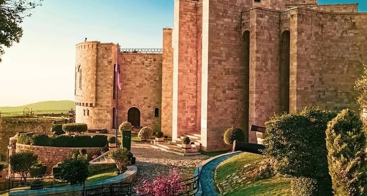 Stone castle with manicured gardens under a clear sky.