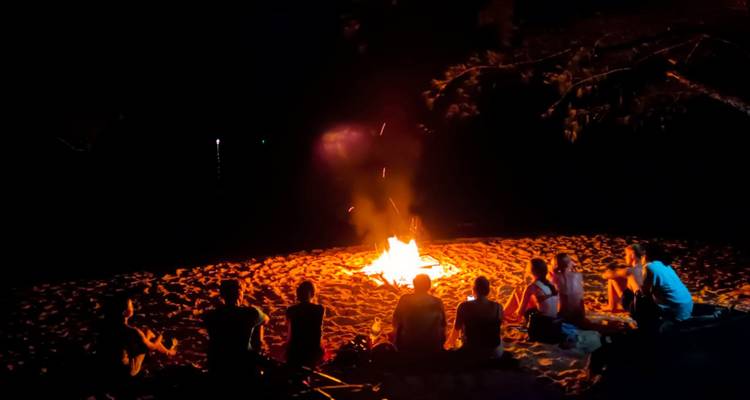 People sitting around a beach bonfire at night.