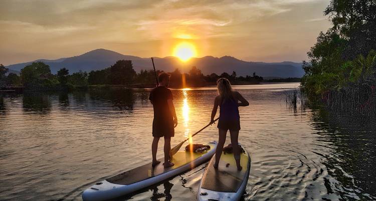 Two people paddleboarding on a lake in front of a sunset.