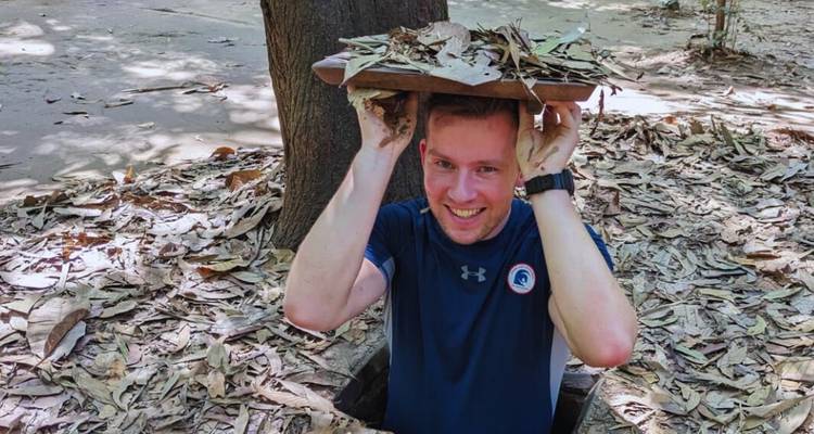 Person, die aus einem Tunnel in einem Wald hervorkommt und eine Holzabdeckung hält.