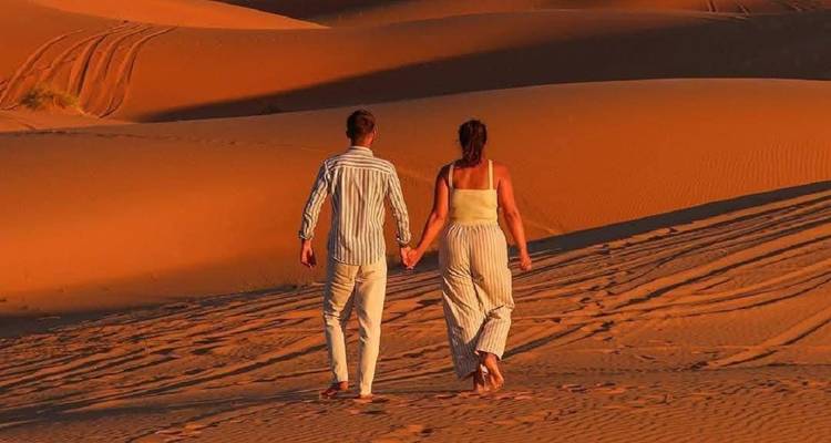 Couple walking through sand dunes under a blue sky.