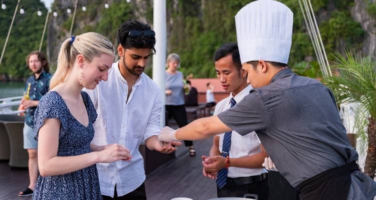 Menschen, die mit Köchen auf einem Bootsdeck mit malerischer Aussicht interagieren.