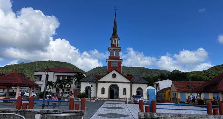 Church with a tall steeple in a quaint town square with mountains in the background.