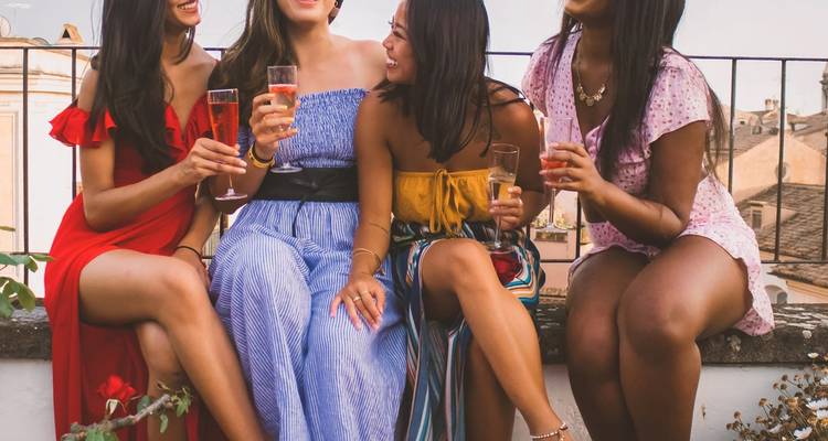 Cuatro mujeres jóvenes vestidas elegantemente, riendo y brindando con bebidas en una terraza de azotea.