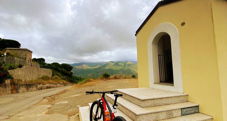Kleine kapel naast een fiets met uitzicht op heuvels.