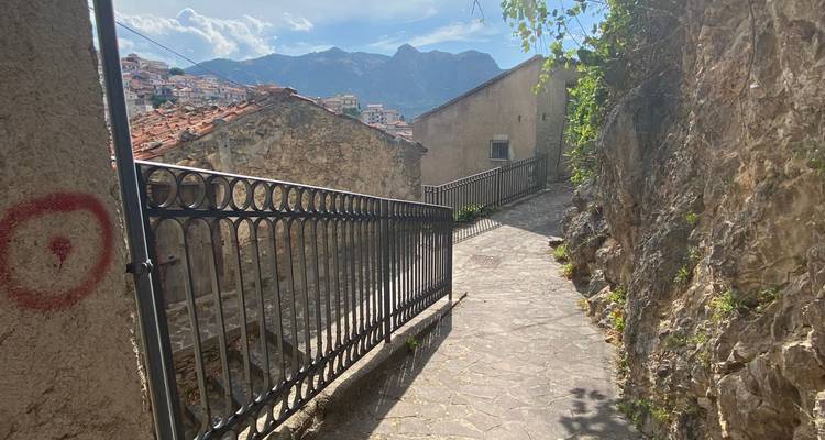 Een smal pad tussen stenen gebouwen met uitzicht op een vallei.
