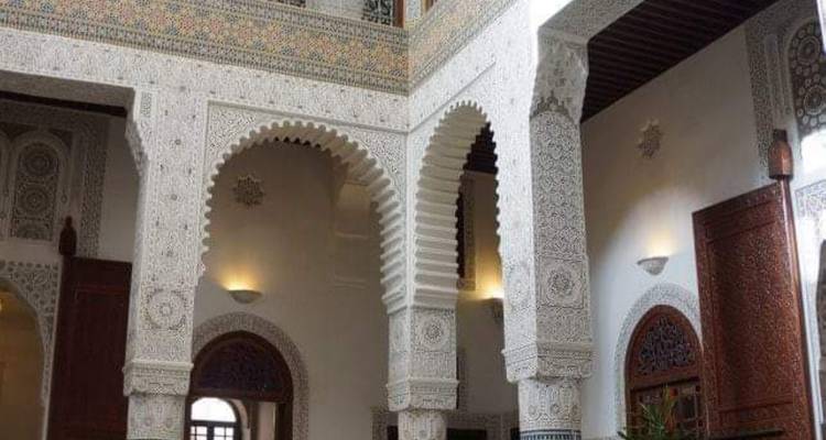 Une cour intérieure ornée avec des arcs en stuc sculpté et un carrelage en mosaïque complexe éclairée par des lampes tamisées.