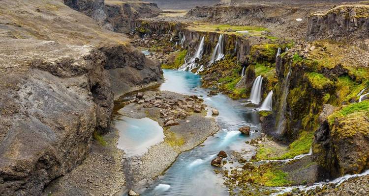 Dramatische kloof met meerdere watervallen die naar beneden storten in een turquoise rivier tussen met mos bedekte basaltwanden.