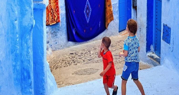 Zwei Kinder, die in einer hellblauen Gasse in Chefchaouen spazieren gehen.