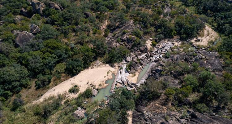 Vue aérienne d'un ruisseau sablonneux serpentant à travers une forêt rocheuse dans un paysage africain