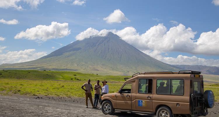 Menschen, die neben einem Safari-Fahrzeug stehen, mit einem Berg im Hintergrund.