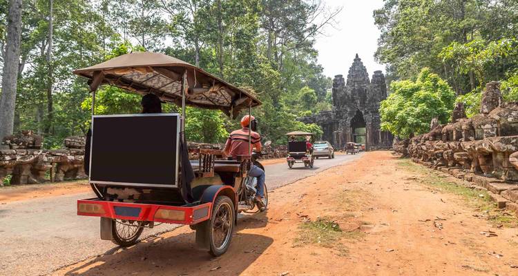 Tuk-tuks on a road with an ancient gateway surrounded by trees.