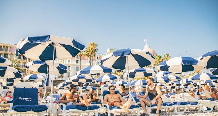 Menschen, die an einem Strand mit ikonischen Sonnenschirmen in Nizza entspannen.