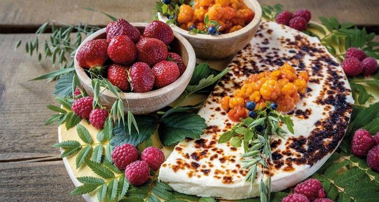 A platter of cheese with berries and herbs.