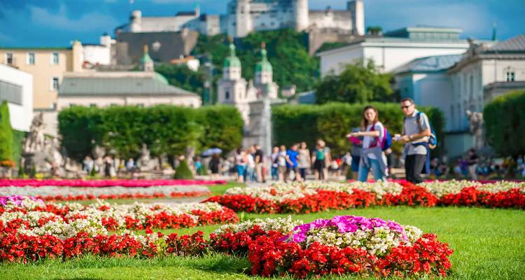 Un jardin avec des fleurs colorées et des gens en arrière-plan avec un paysage urbain historique.