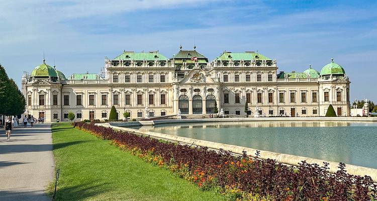Un grand palais avec un étang serein et des fleurs au premier plan.