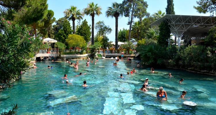 Überfülltes Thermalbad mit Schwimmern, umgeben von üppigem Grün.