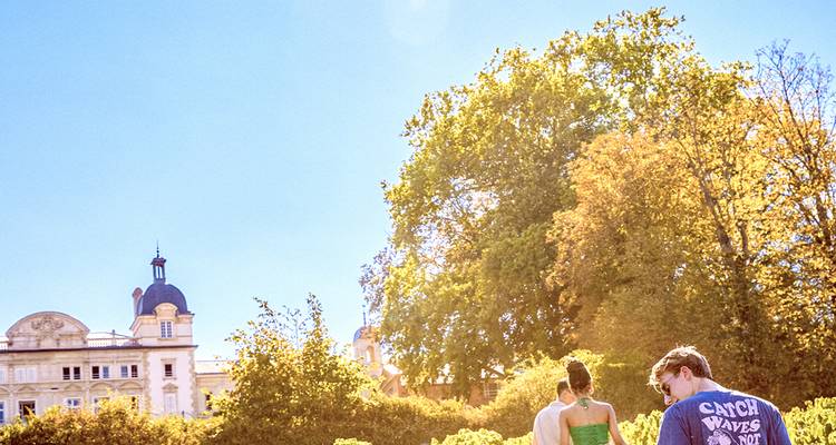 Los viajeros exploran jardines soleados junto a un gran castillo francés en la región vinícola de Beaujolais