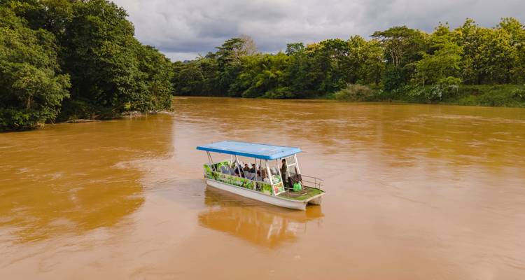 Toeristenboot op een bruine rivier omgeven door weelderige vegetatie.