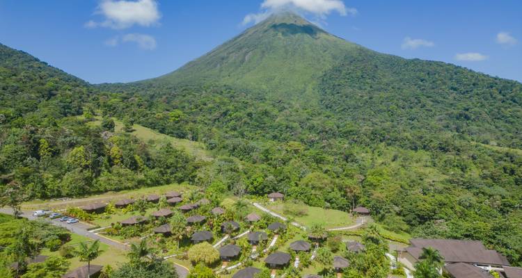 Landschap met verspreide hutten en een vulkaan op de achtergrond.