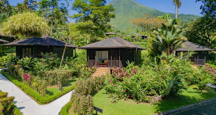 Groene bungalows omringd door tropische tuinen met een vulkaan op de achtergrond.