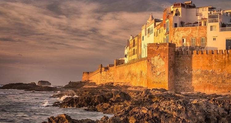 Sonnenuntergang über einer Festung am Meer und Wellen, die gegen die Felsen krachen.