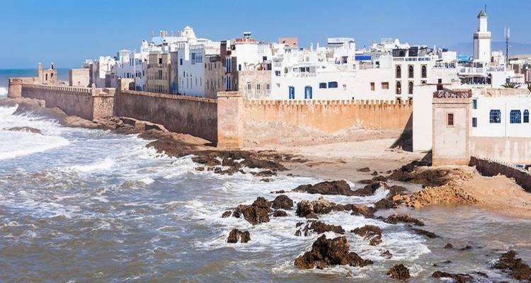 Stadtmauern und Meereswellen, mit einem Leuchtturm in der Ferne sichtbar.