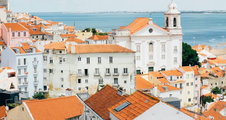 Vue panoramique des toits en terre cuite de Lisbonne et d'une église blanche au sommet d'une colline surplombant le Tage.