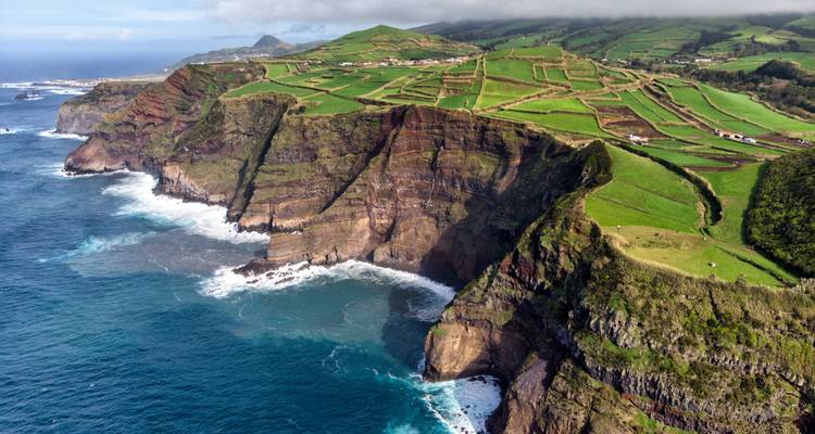 Vue aérienne des falaises vertes spectaculaires et des champs en damier qui s'étendent jusqu'aux eaux turquoise de l'Atlantique sur l'île de São Miguel.